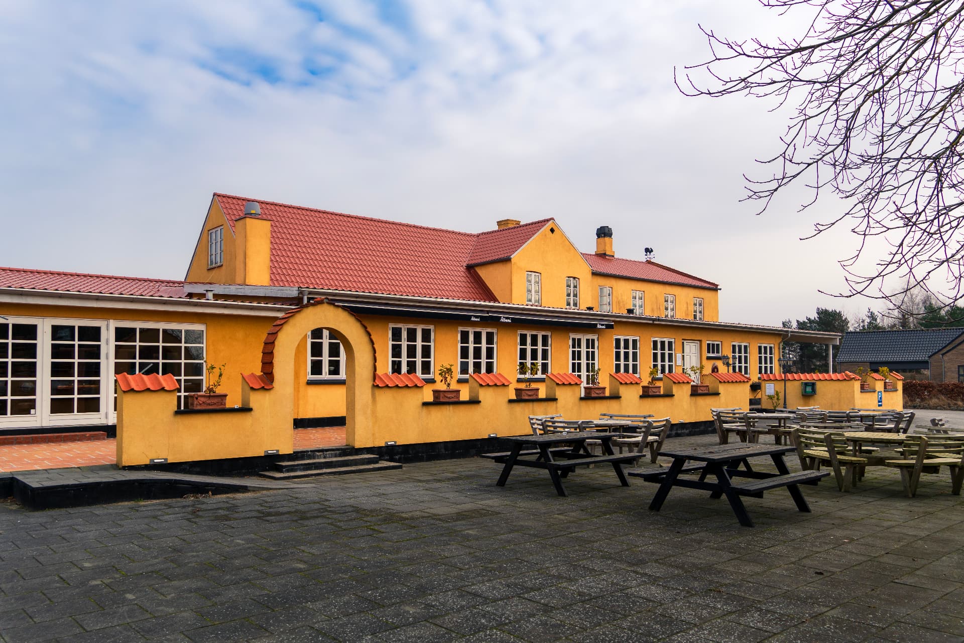 Orø Kro & Hotel set udefra med gul facade, rødt tegltag og bænkeborde