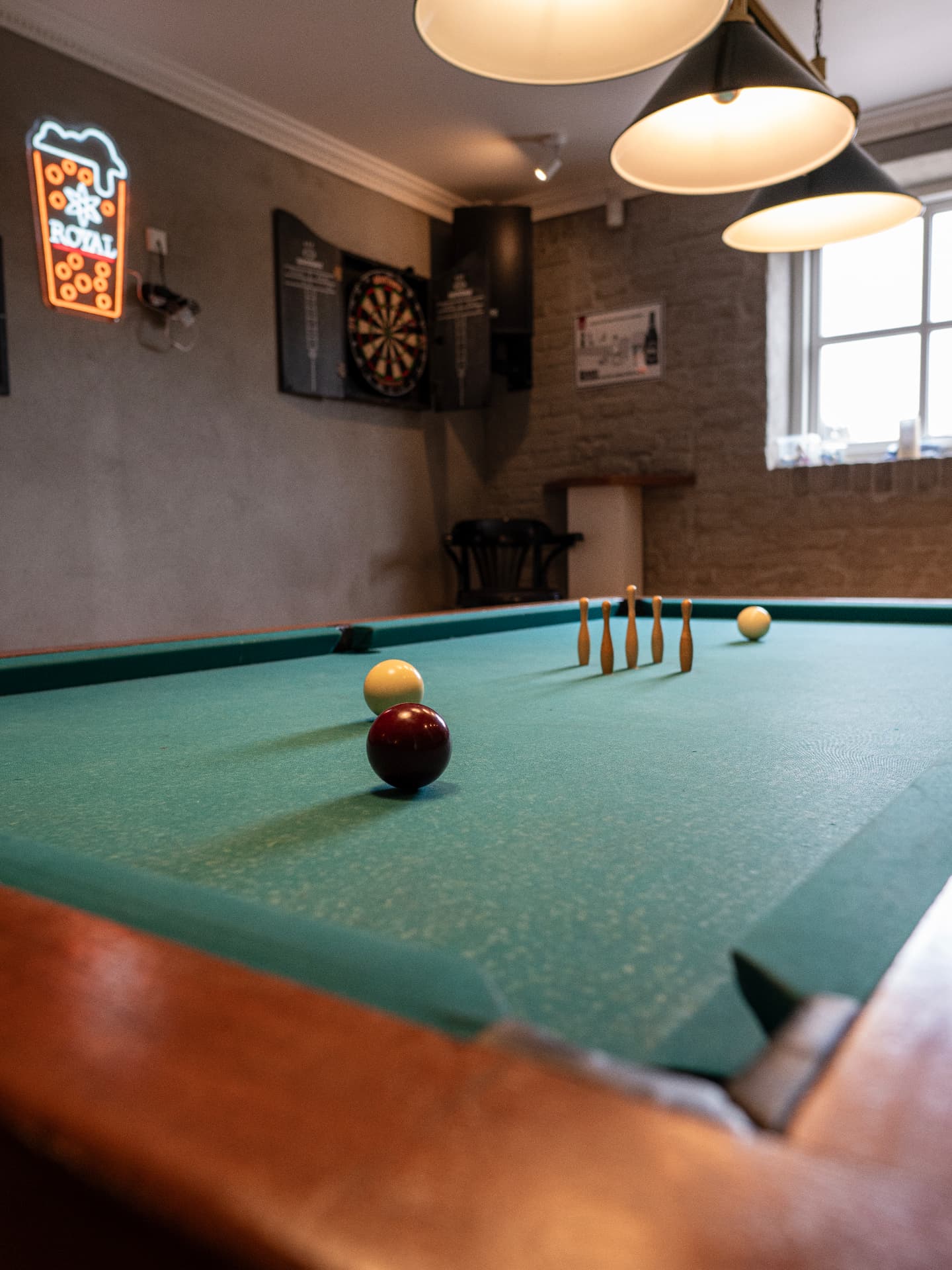 Poolbord med keglespil, dartskive og neonskilt i kroens spillerum
